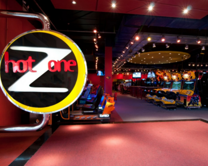 Foto da entrada do Hot Zone, um espaço fechado com iluminação vermelha e brinquedos estilo arcade. Na entrada, um letreiro luminoso grande com o Z do Hot Zone em destaque